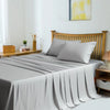 A light gray bamboo fiber flat bed sheet draped over a wooden bed with white pillows and a yellow abstract painting in the ba