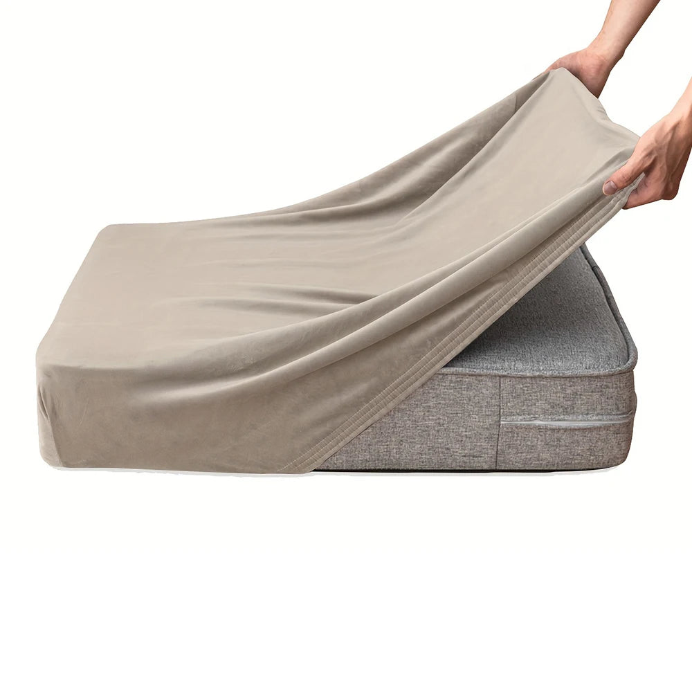 A hand is draping a beige velvet stretchy sofa seat cover over a gray sofa cushion.