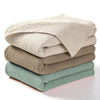 Stack of beige and olive green cotton gauze blankets folded neatly