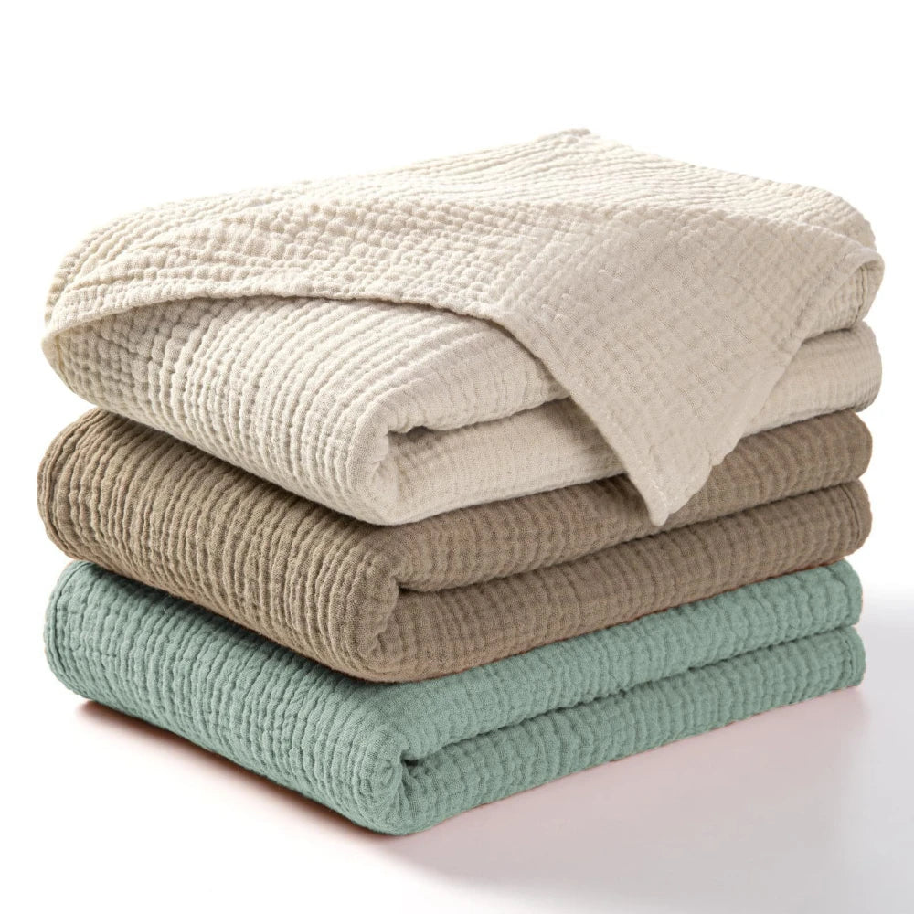 Stack of beige and olive green cotton gauze blankets folded neatly