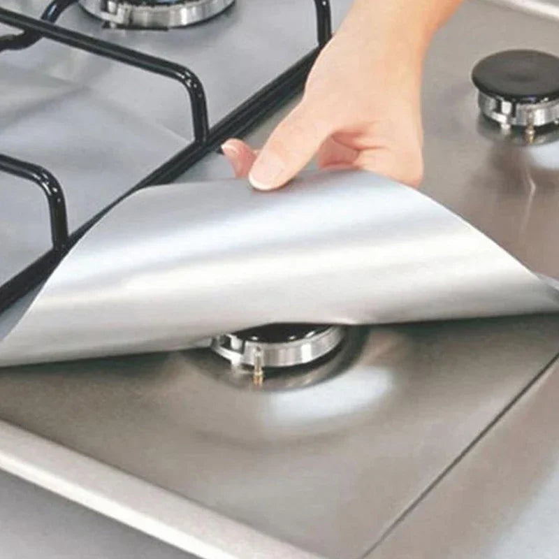 A hand places a silver reusable gas hob protector liner onto a stovetop burner.