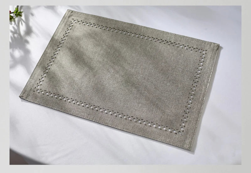 A rectangular linen placemat in a light gray color with decorative hand embroidery.