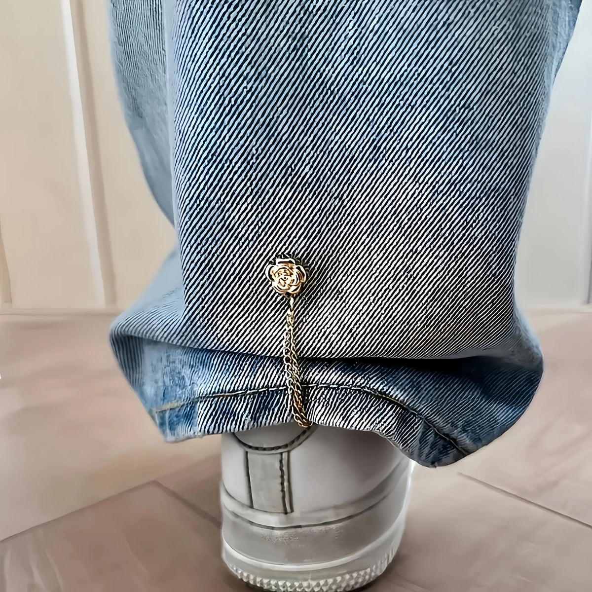 Close-up of denim jeans cuff featuring a gold magnetic chain buckle detail.