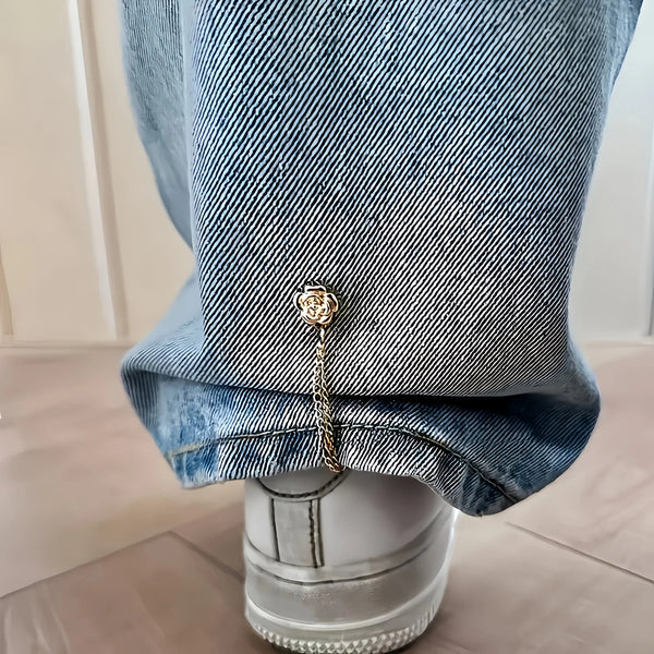 Close-up of denim jeans cuff featuring a gold magnetic chain buckle detail.