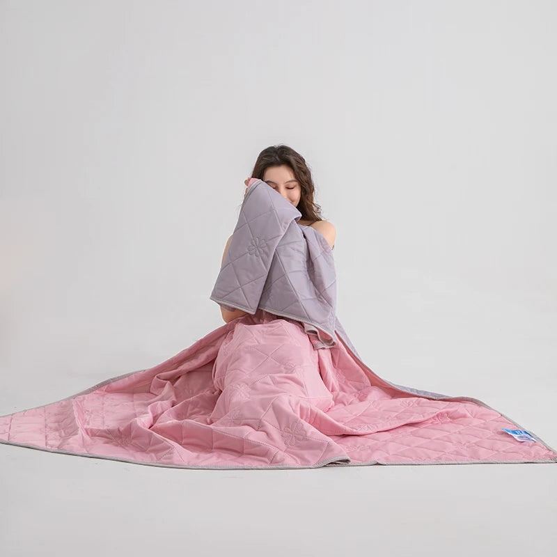 A woman is wrapped in a pink lightweight cooling blanket, showing the soft texture and drape of the fabric.