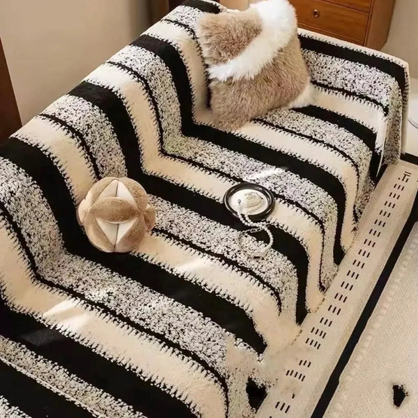 A bohemian striped sofa cover featuring black and cream stripes with a fluffy accent pillow.