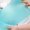 A hand is placing a blue silicone fridge and drawer liner onto a white porcelain sink or basin.