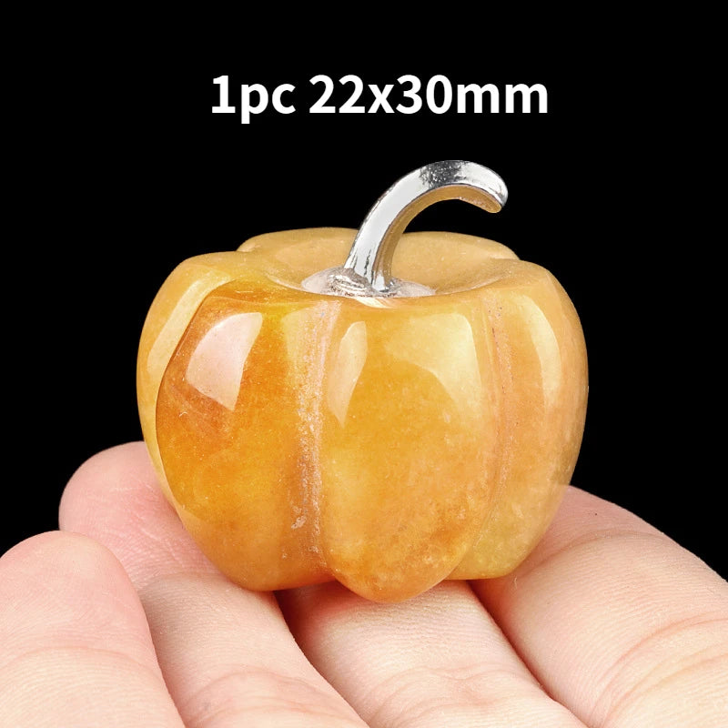 A small, smooth, orange-yellow natural stone pumpkin figurine with a silver stem is held in a hand.