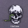A black and white embroidered skull with a green snake coiled around its head on a gray fabric background.