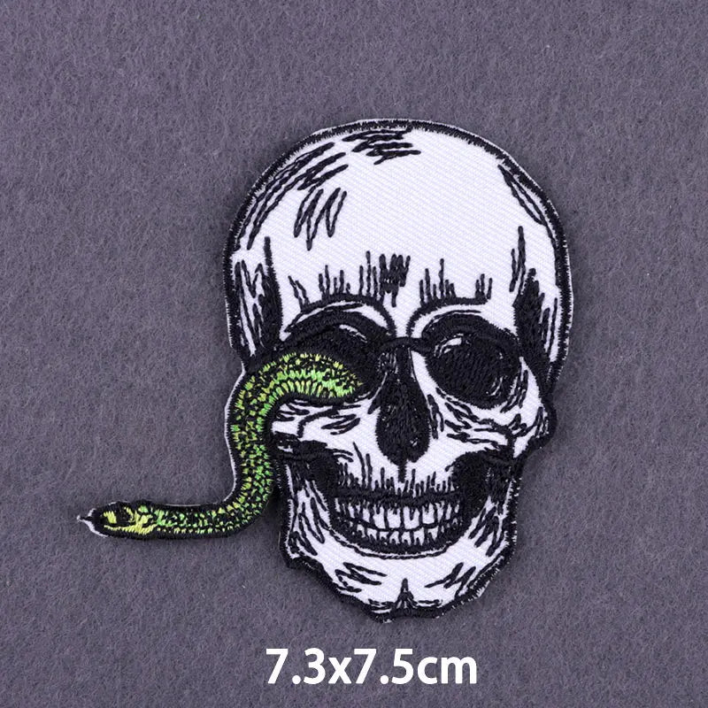 A black and white embroidered skull with a green snake coiled around its head on a gray fabric background.