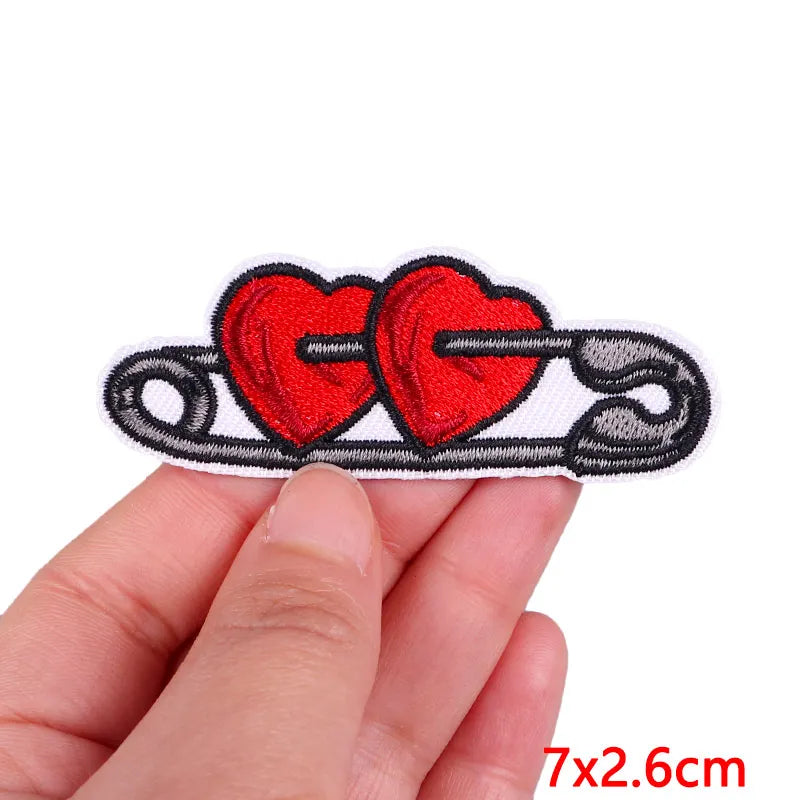 A hand holds a red heart embroidered patch shaped like a cartoon cat with a tail and whiskers.