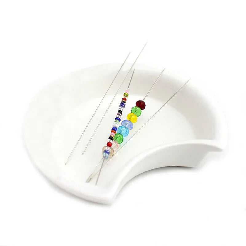 A set of precision stainless steel beading needles with colorful beads displayed on a white dish.
