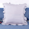 A light lavender ruffled pillow cover displayed on a blue fabric surface.