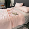 A pink reversible cooling quilt is displayed on a bed with white linens and pillows.