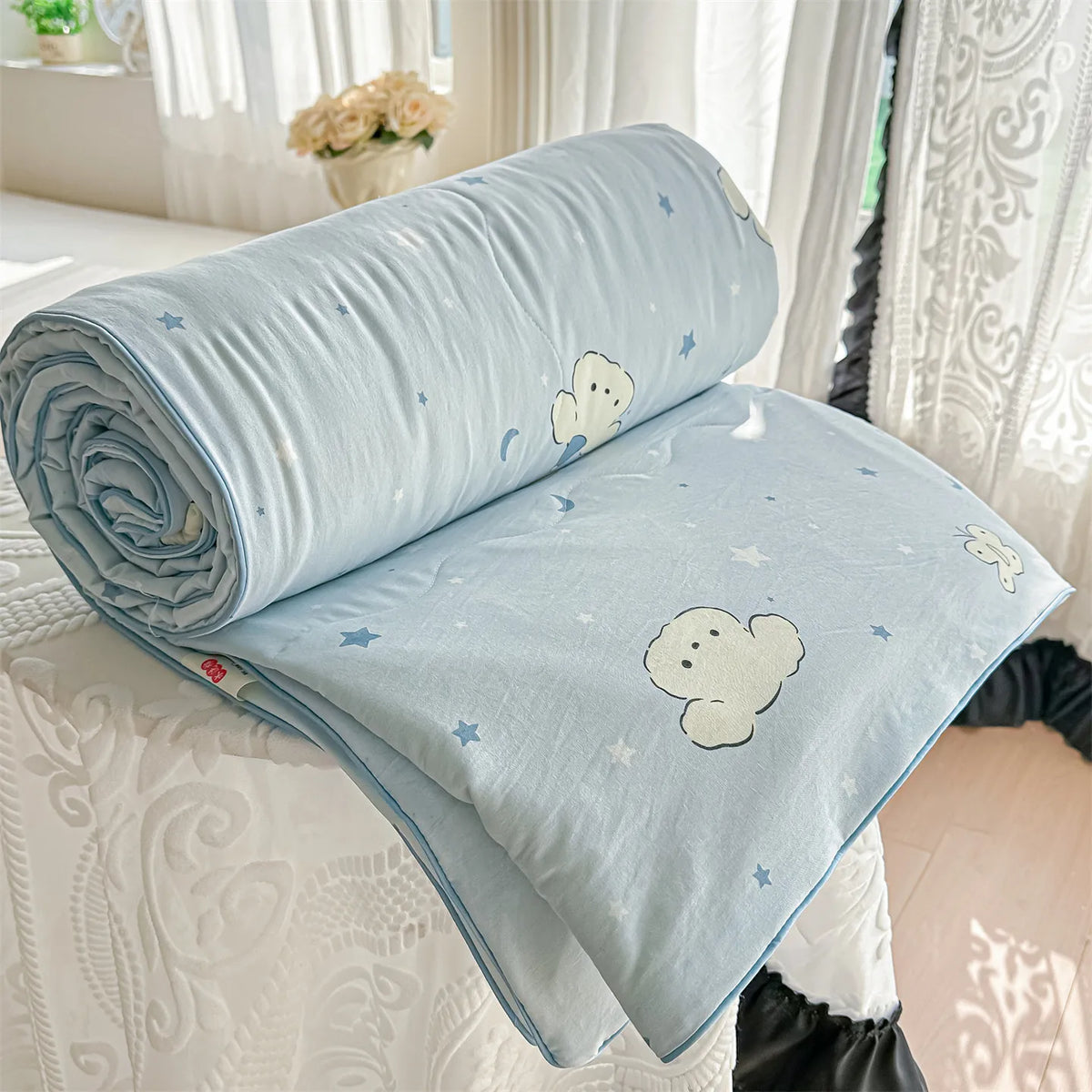 Light blue quilt blanket with white cloud and star patterns rolled up on a white surface.