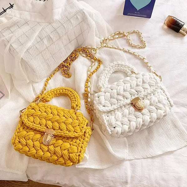 A yellow crocheted handbag and a white crocheted handbag with gold chain straps and metal clasps on a white fabric background