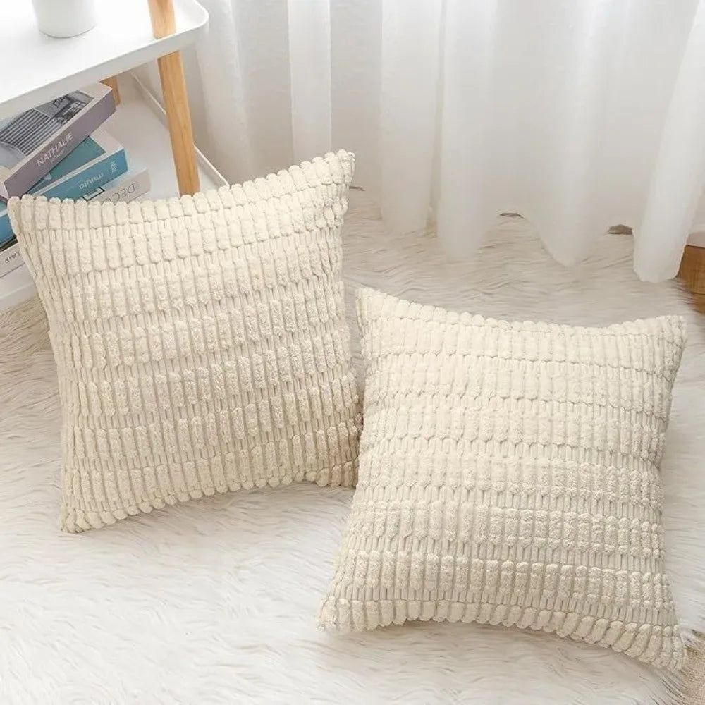 A set of two cream colored, textured knit throw pillows resting on a white surface.