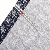 A precision metal sliding sewing gauge with a red marker is shown diagonally across a gray fabric.