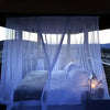A large white mosquito net draped over a bed in an outdoor setting, illuminated by soft light.