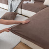 A hand touches a brown ribbed sofa cushion cover on a white rug.