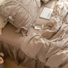 A close-up of a beige princess ruffle cotton bedding set with a clear glass bottle and a book on a light pink surface.