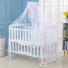 White crib with a sheer pink mosquito net draped over it in a light blue room.