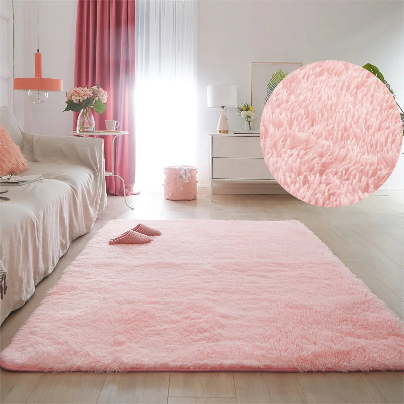 A fluffy pink shag rug is laid on a light wood floor in a bright living room with sheer curtains and white furniture.