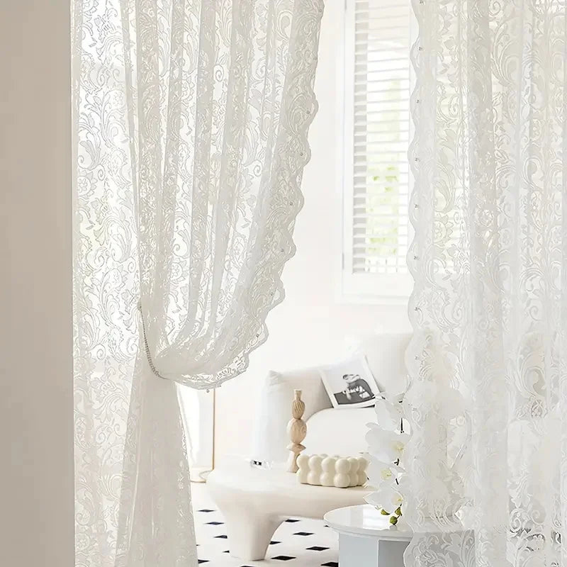 White lace curtain with a beaded phoenix tail design hanging in a bright room.