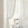 White lace curtain with a beaded phoenix tail design hanging in a bright room.