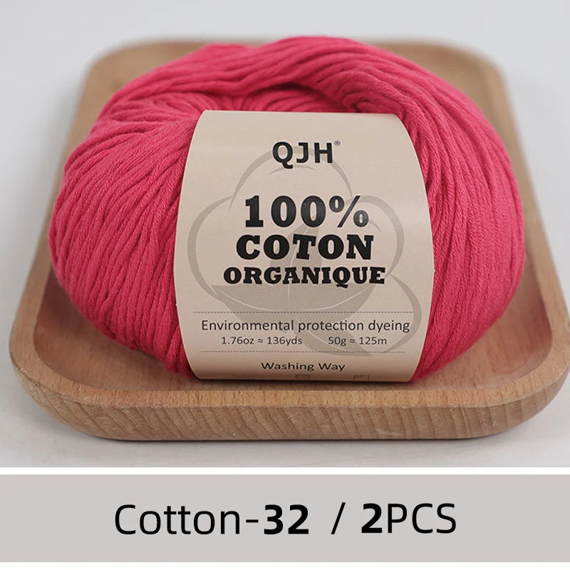 A ball of pink organic cotton yarn labeled QJH 100% COTON ORGANIQUE resting on a wooden tray.