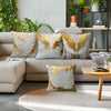 A collection of decorative throw pillows featuring golden and white wing patterns on a light beige sofa.
