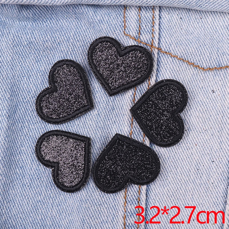 Five black glitter iron-on embroidered love heart star patches on a light blue denim fabric.