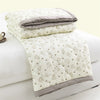 A white quilted duvet cover with a light floral pattern and gray trim, folded on a white bed.