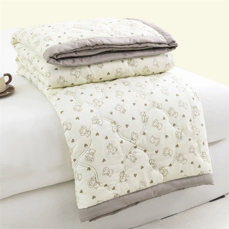 A white quilted duvet cover with a light floral pattern and gray trim, folded on a white bed.