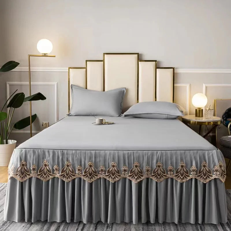 A bed with a gray embroidered cotton bedspread and pillows against a light wall backdrop.