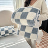 A person holds a thick gray and white checkered flannel fleece blanket in a cozy indoor setting.