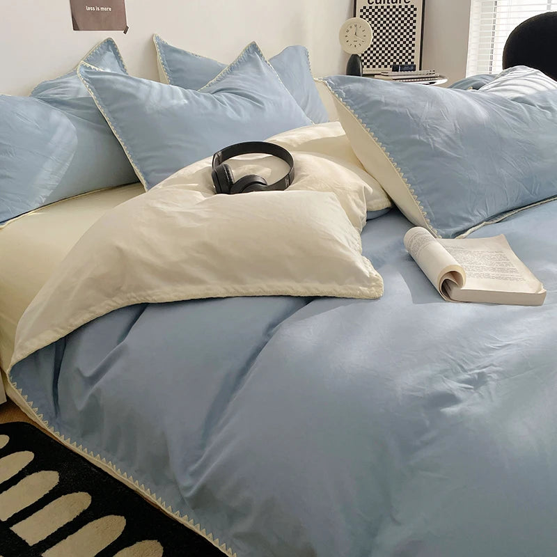 A bed with light blue and cream linen bedding, pillows, and a book on the surface.