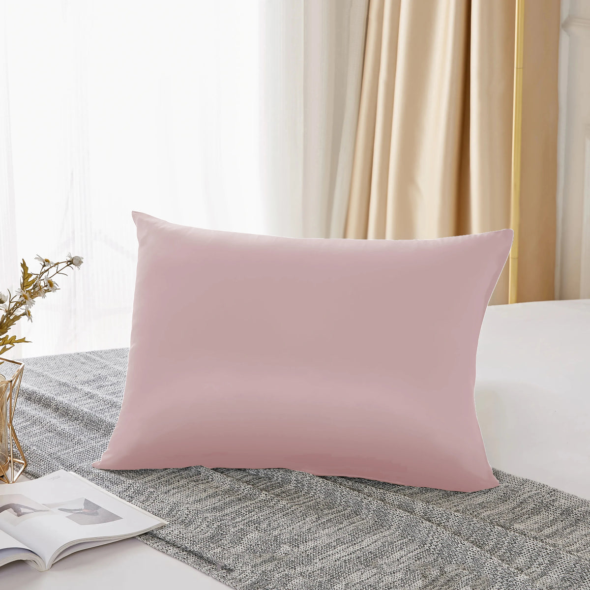 A pink silk pillowcase resting on a gray textured fabric next to a window.