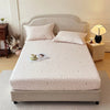 A white floral printed cotton fitted sheet is displayed on a bed with light gray bedding and a upholstered headboard.