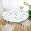 A round white vinyl tablecloth with a floral pattern is set on a wooden table surrounded by white chairs.