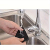 A hand is using a black non-slip carpet gripper to suspend and drain water from a kitchen faucet.