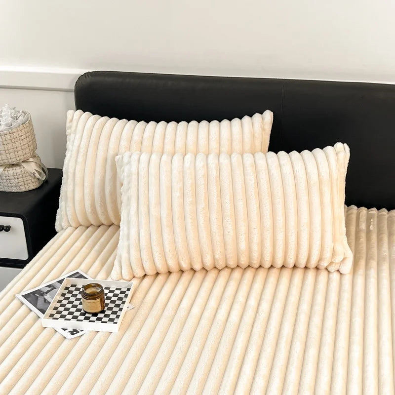 A close-up of thick, cream-colored fitted bed sheets with vertical pleats resting on a light-colored bed.
