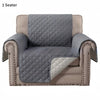 A single gray quilted slip-on protective sofa cover in a beige fabric.