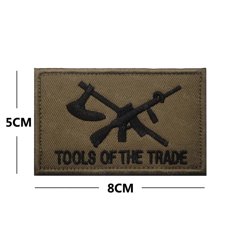 A rectangular brown embroidered patch featuring a black crossed tool design and the text TOOLS OF THE TRADE.