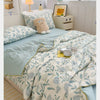 A light blue and white patterned quilt with a pale green trim is displayed on a bed, next to a yellow lamp.