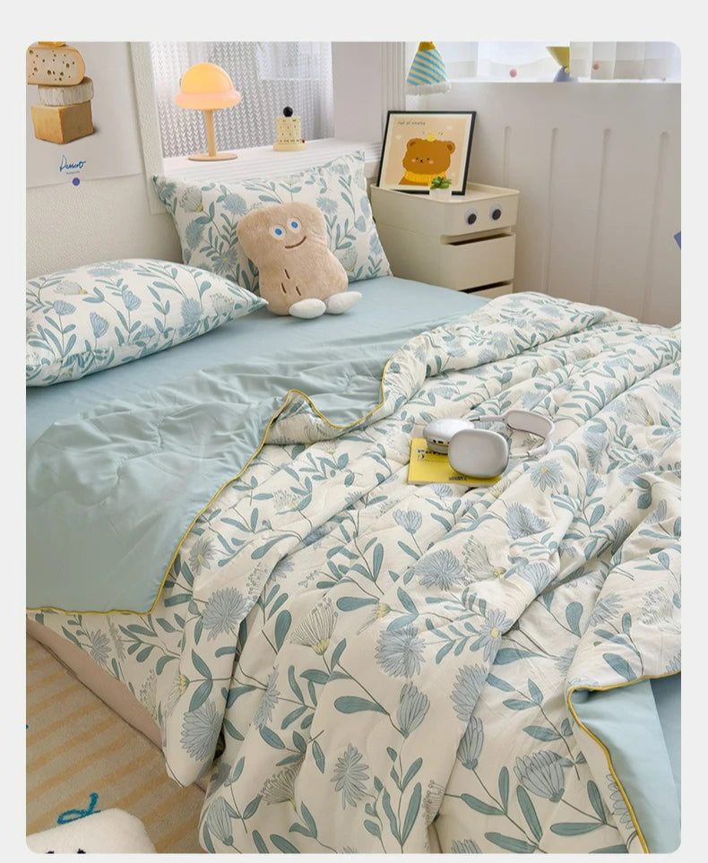 A light blue and white patterned quilt with a pale green trim is displayed on a bed, next to a yellow lamp.