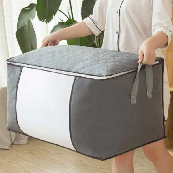 A person holds a gray quilted storage bag with white panels, designed for portable clothing and quilt storage.