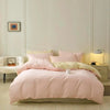 A pink duvet cover set with pillows and a matching pink bedspread on a light wood floor.