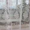 Sheer white embroidered curtains with floral designs covering a window.