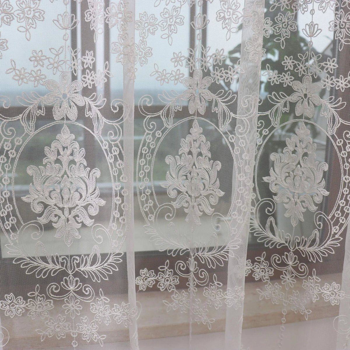 Sheer white embroidered curtains with floral designs covering a window.